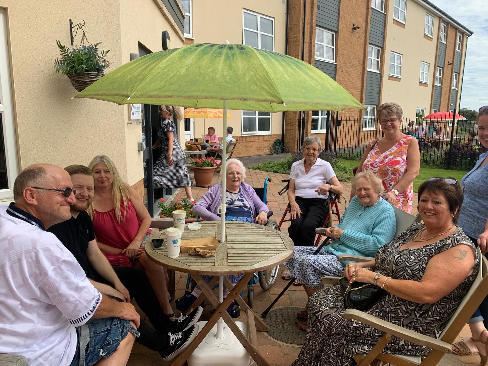 Elderly residents gathered at a table, smiling and enjoying the festivities of a summer fair at Tanglewood care home.