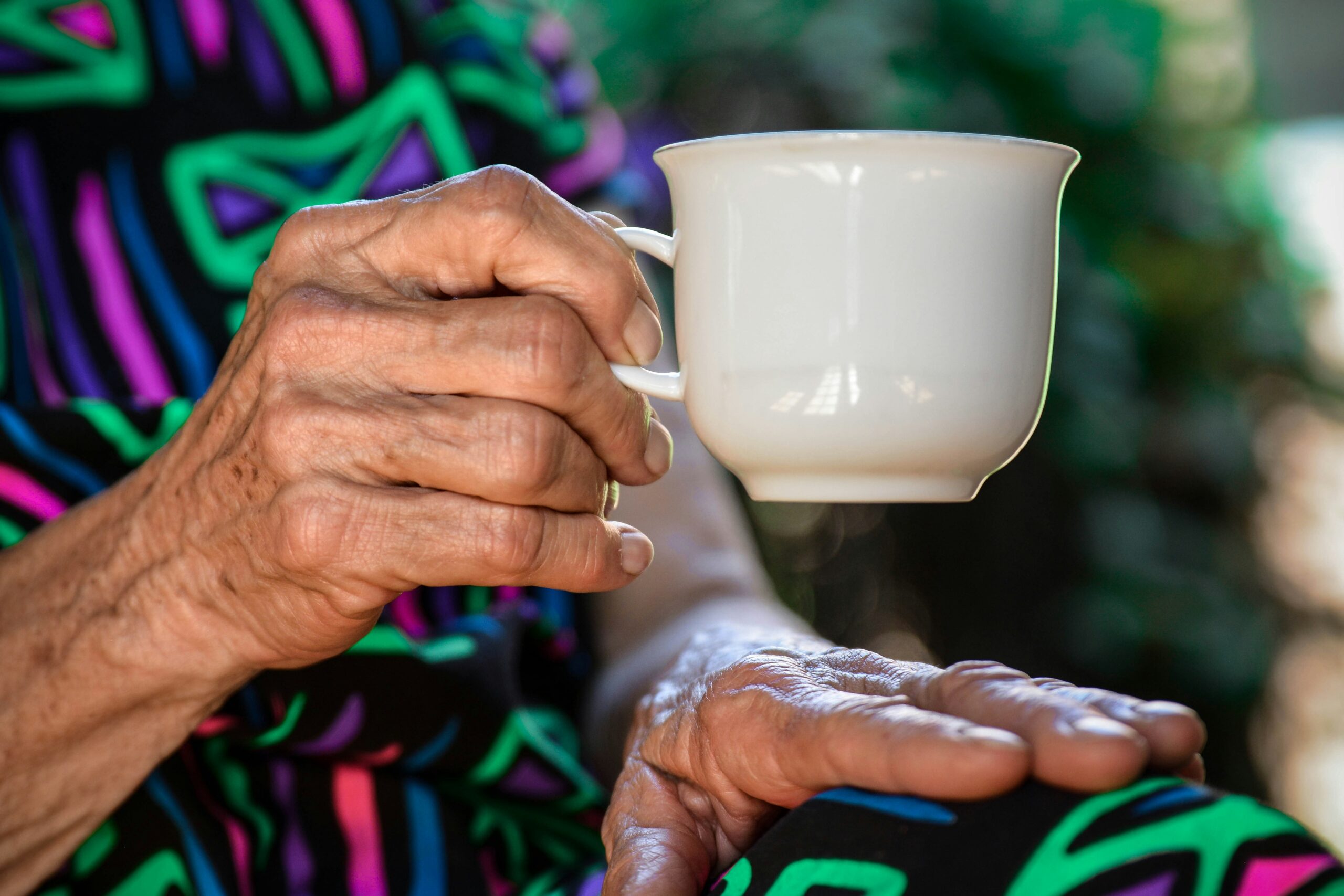 An elderly woman's hand with soft wrinkles holding a delicate cup of tea, symbolizing relaxation and comfort.