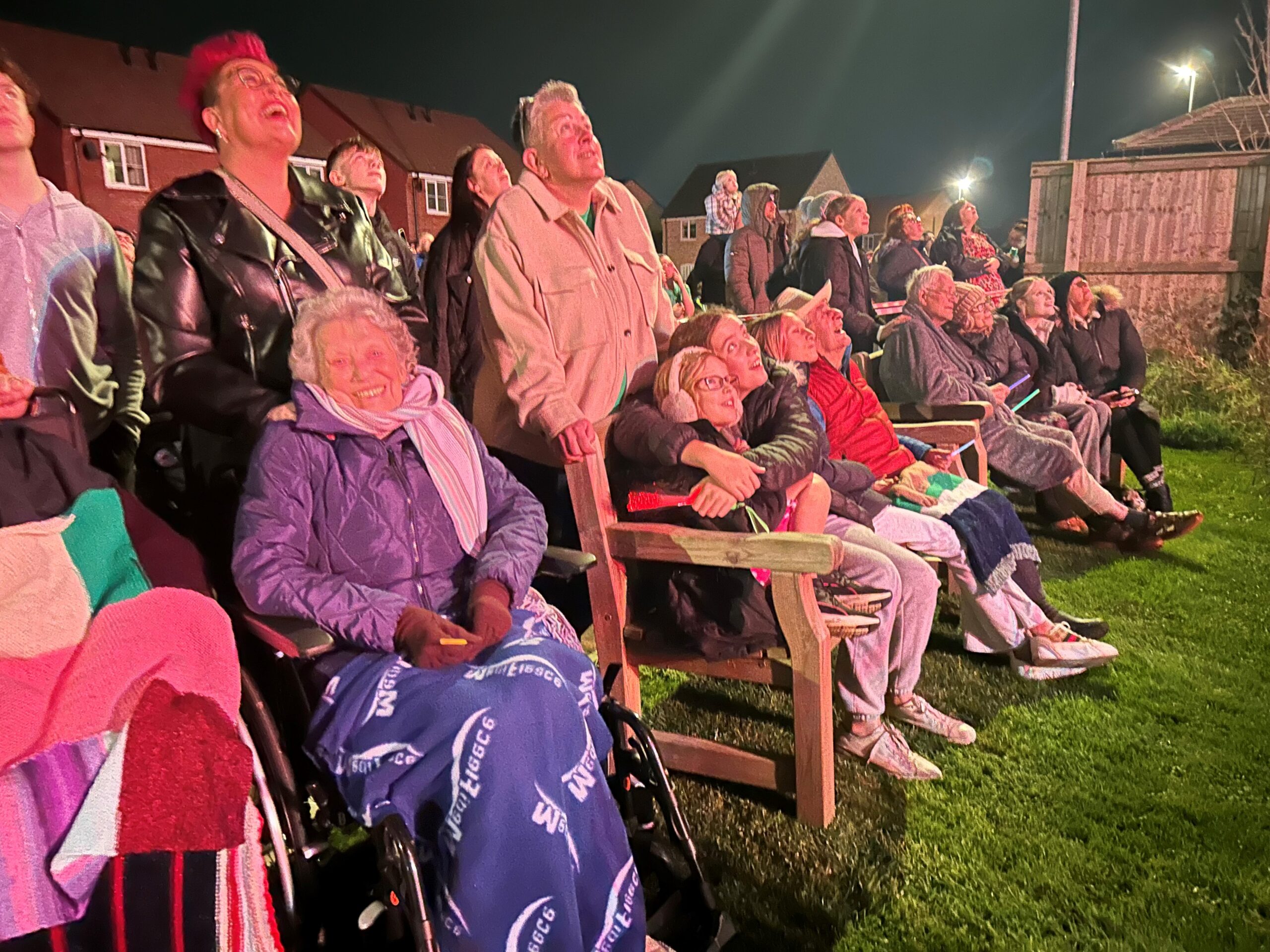 A group of residents and family members gathered outdoors at Tanglewood Care Homes, watching a vibrant fireworks display light up the night sky.