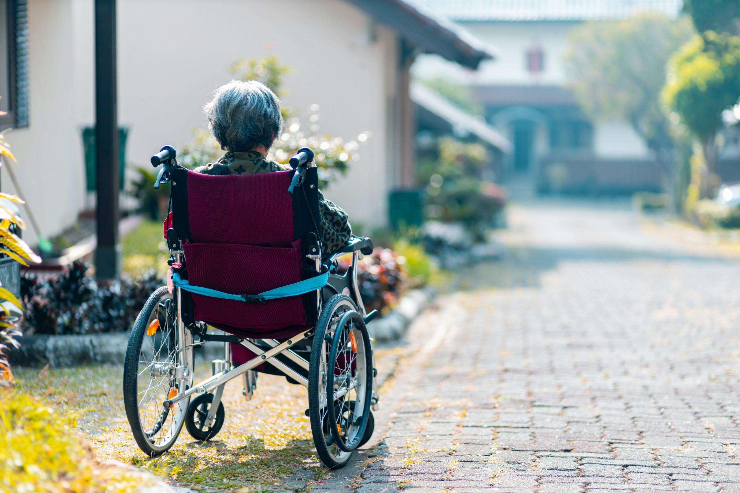 Elderly woman looking out a cobbled road, whilst sat in a wheelchair. 