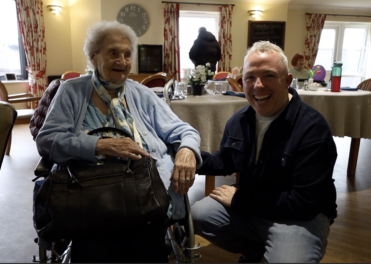 John Sweeney, from Drop Dead Generous, sitting beside a resident at Cloverleaf Care Home.